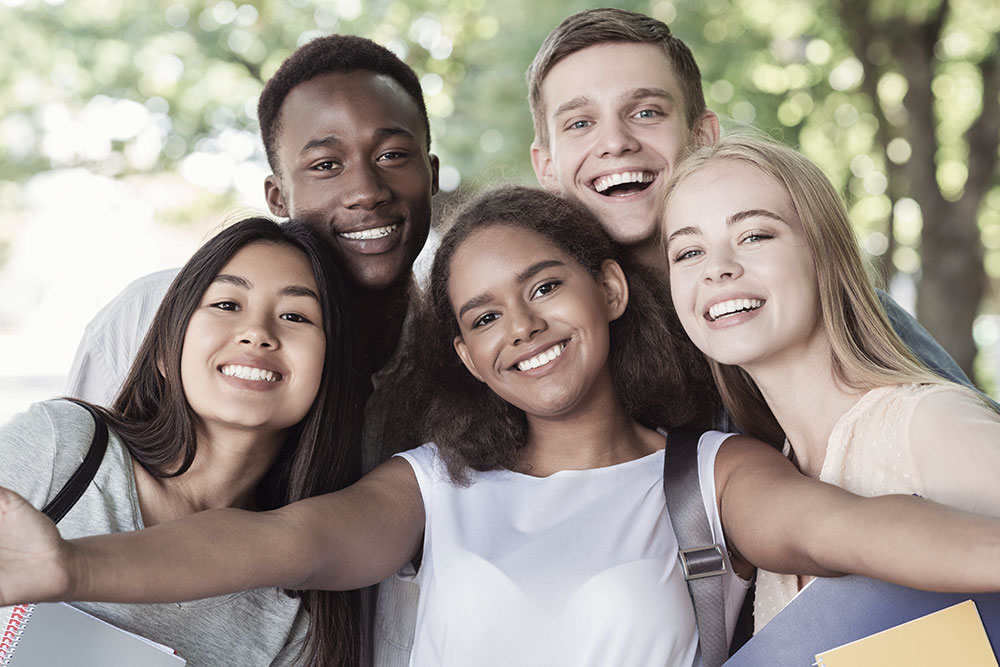 Cheerful international friends teenagers taking selfie while walking in summer park